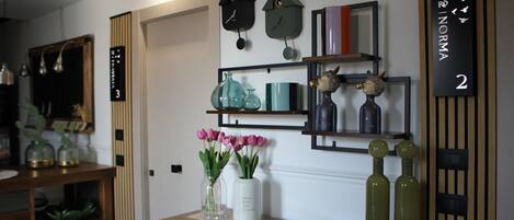 A room with a wooden door labeled '3', a wall-mounted clock, a shelf with decorative items, and a vase with pink flowers.