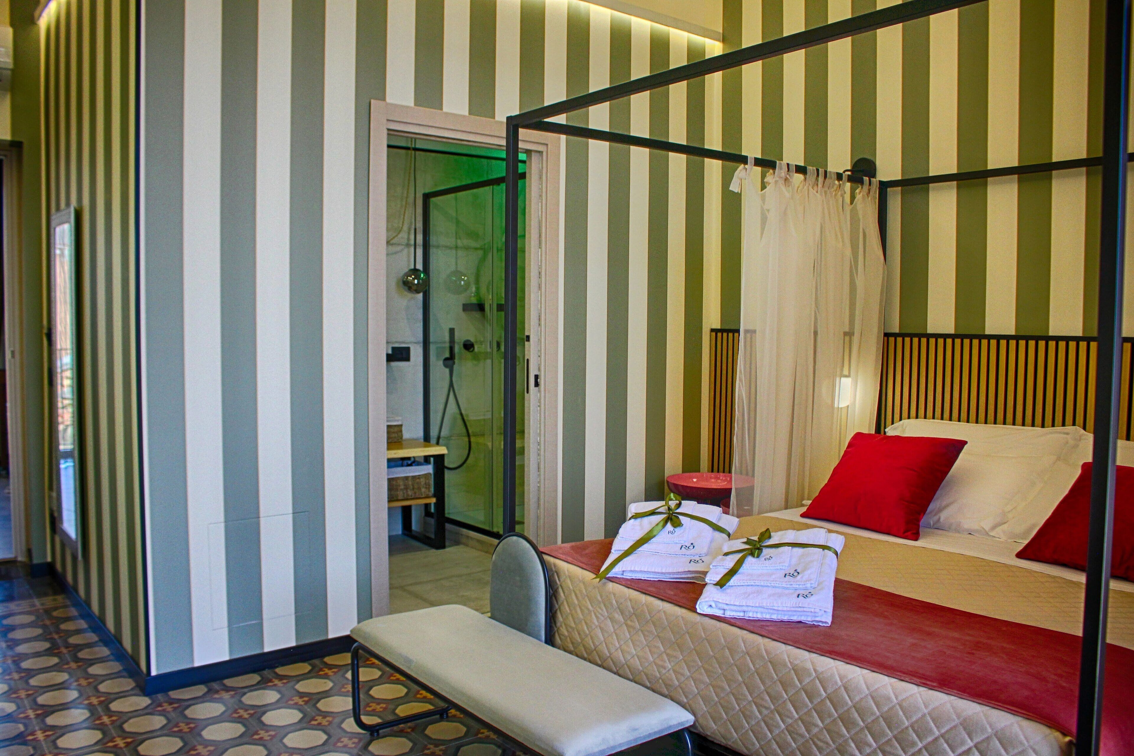 A four-poster bed with red and white pillows, a bench, and a bedside table with towels.