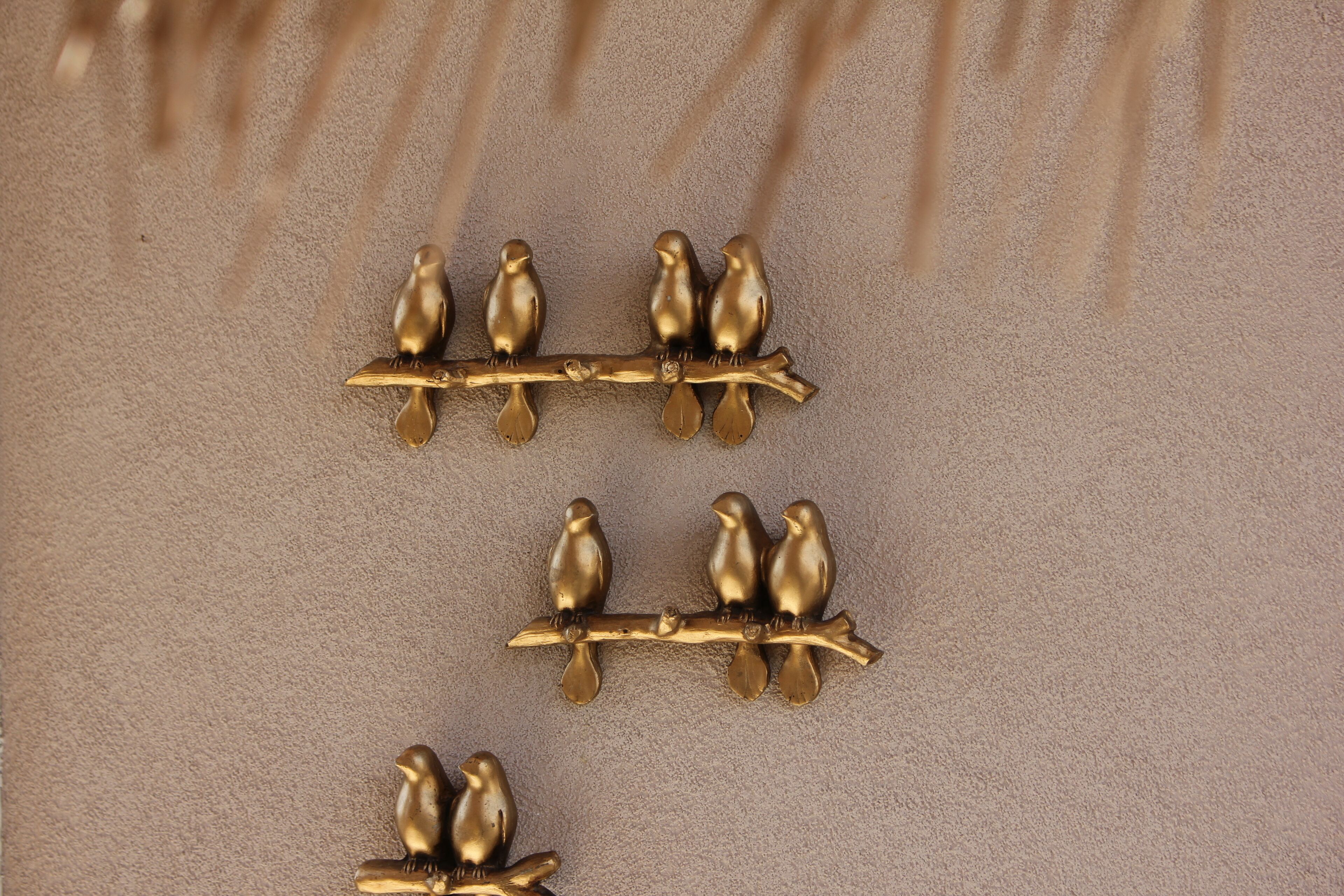 Three gold-colored bird figurines on branches against a textured beige background.