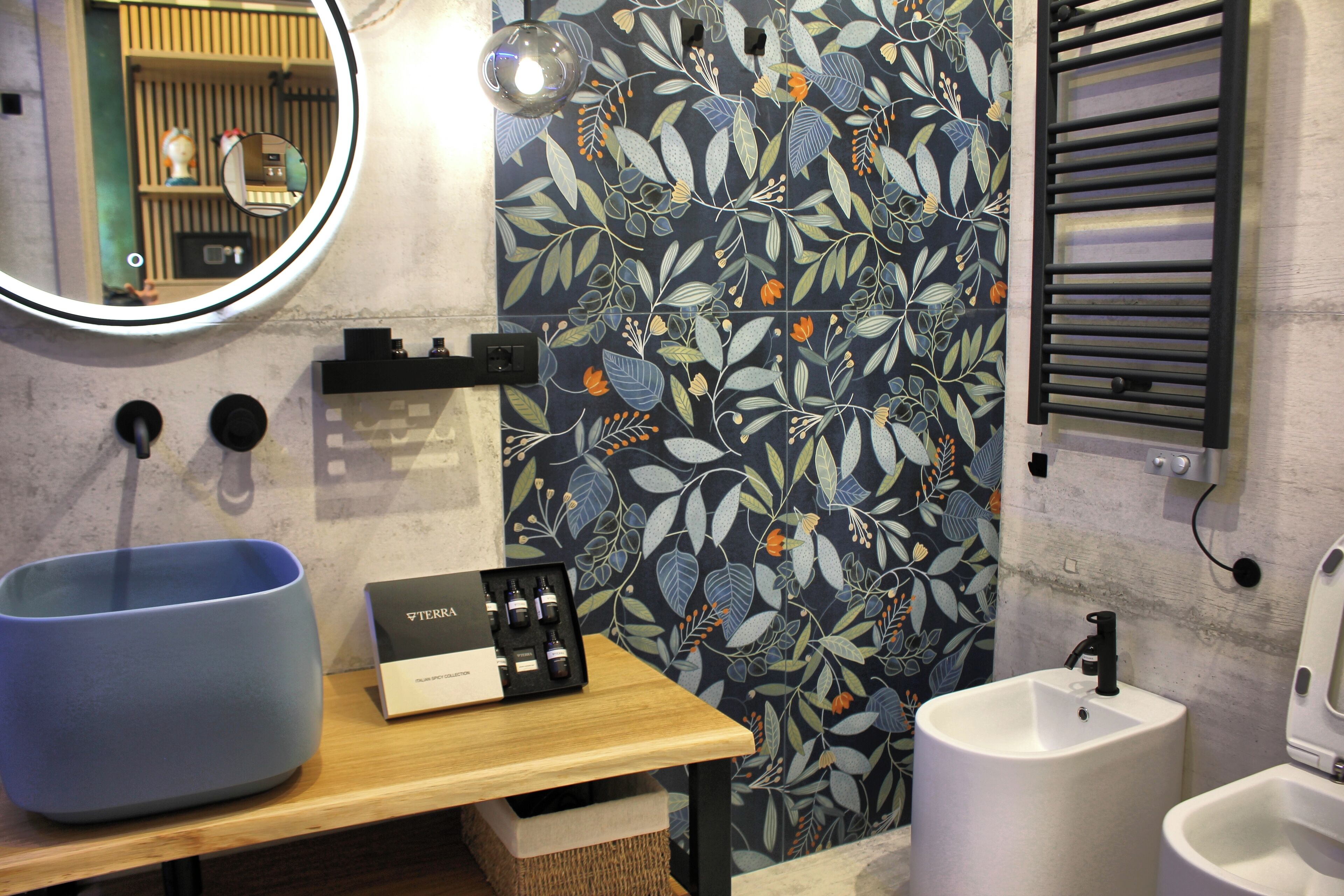 Un baño con un lavabo azul, un lavamanos, un inodoro, un espejo y una pared decorativa con estampado floral.