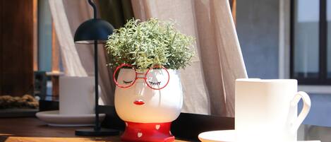 A table with a decorative ceramic cup and saucer, a small potted plant, and a black lamp.