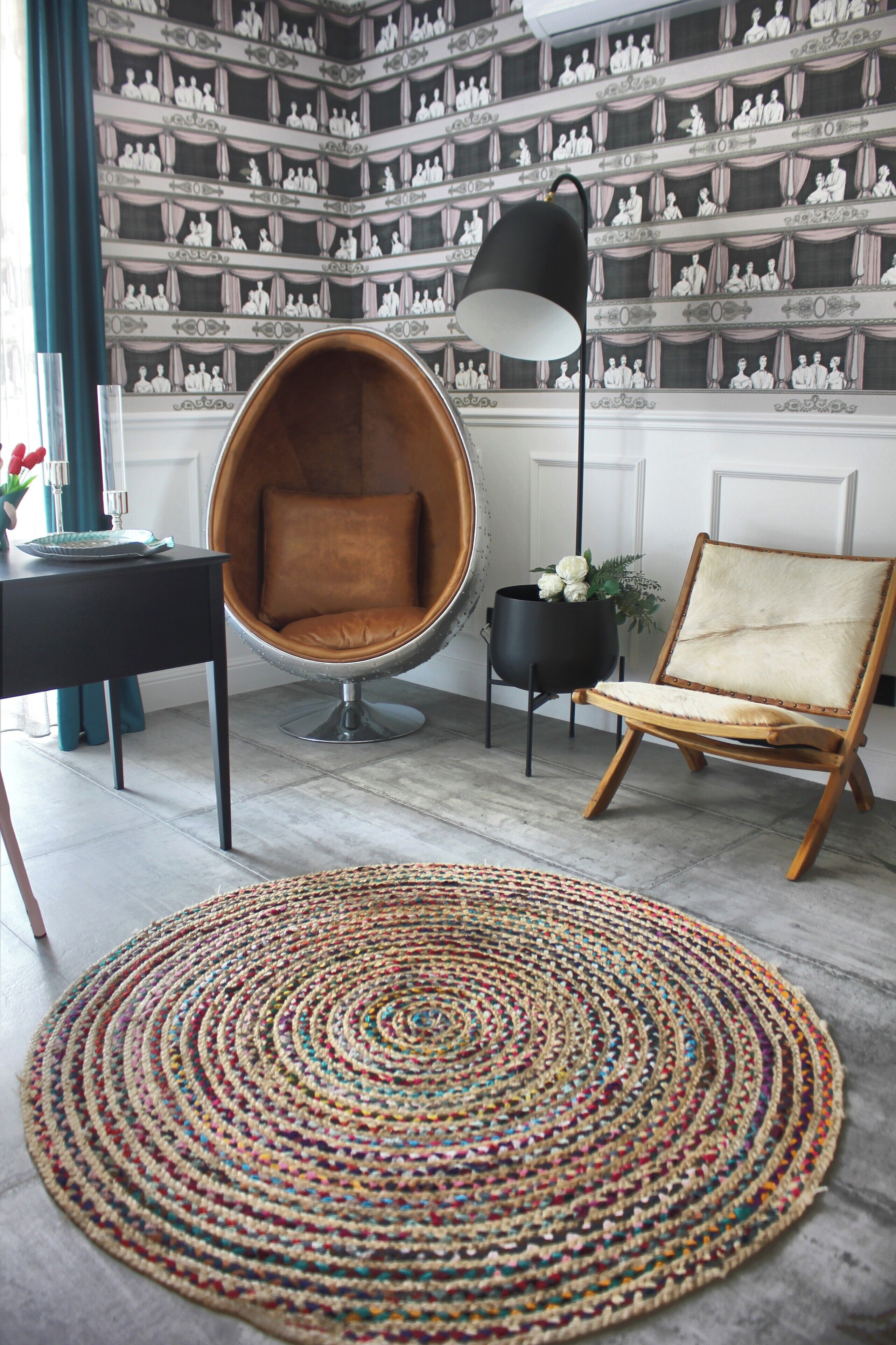 Ein Zimmer mit einem runden gewebten Teppich, einem braunen Ledersessel, einer schwarzen Stehlampe und einer wandgestaltenden Tapete.