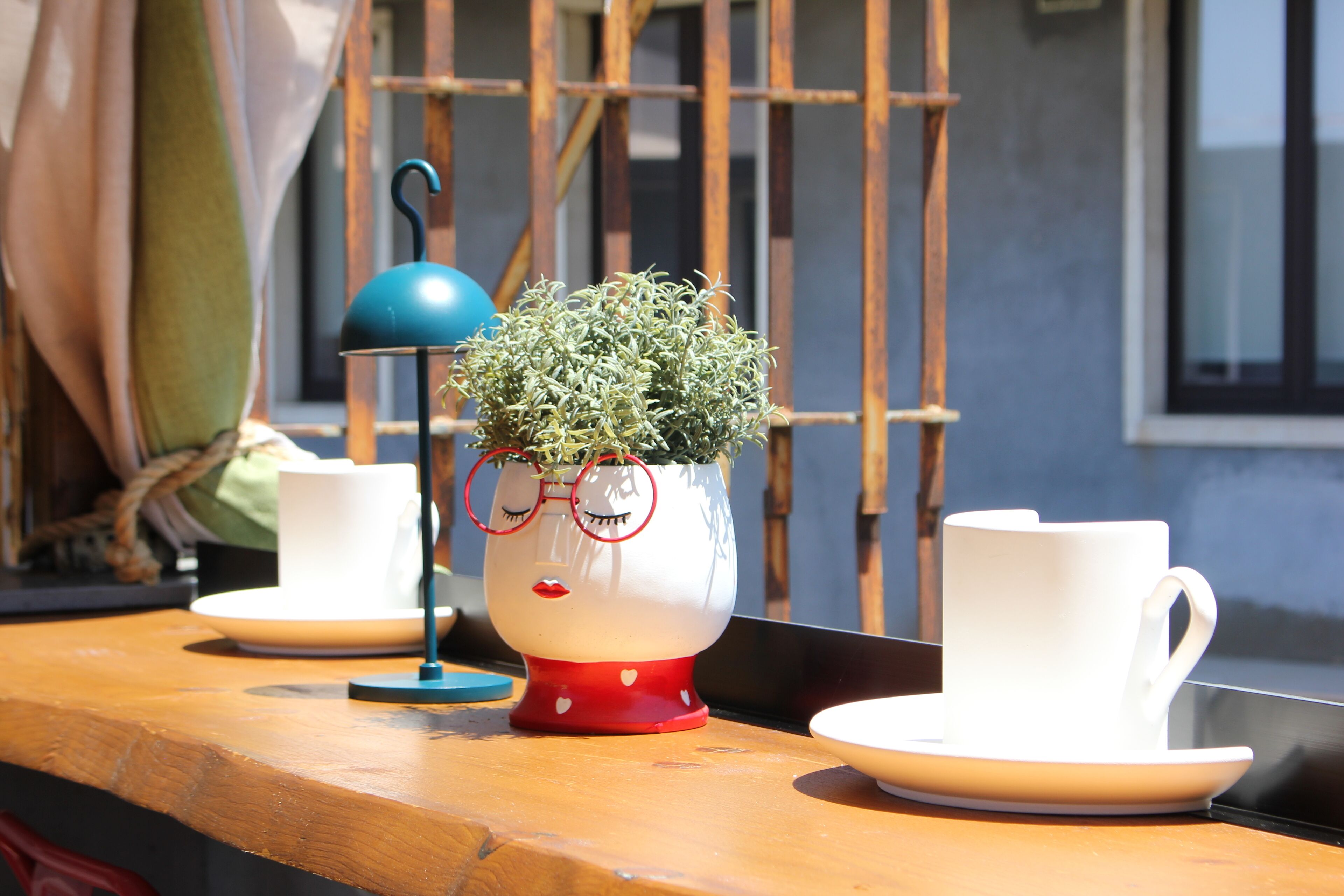 A table with a potted plant, two white cups, and a blue lamp.