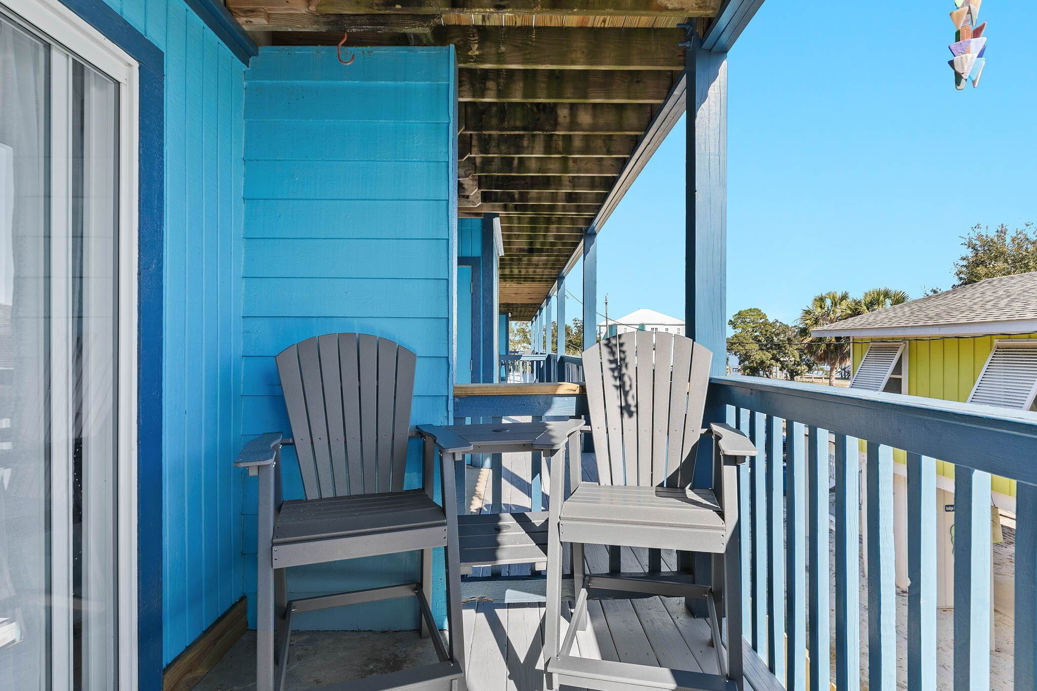 A covered outdoor area with two Adirondack chairs and a small table, a blue building, and a clear sky.