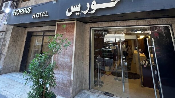 A hotel entrance with a sign in both English and Arabic, a potted plant, and a glass door leading inside. - Houres Hotel (Cairo)