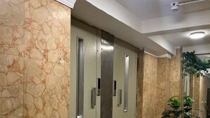 Un couloir aux murs de marbre, avec une poubelle et des plantes en pot.