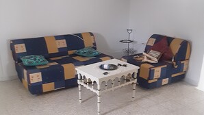 A room with two patterned sofas, a small white table, and a wall-mounted shelf.