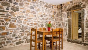 Ein Zimmer mit Steinwänden, einem Holztisch und Stühlen, einer Topfpflanze und einer Tür zu einem anderen Raum.