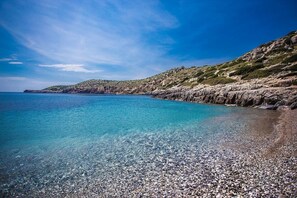 Una vista despejada del litoral, con una playa de guijarros y acantilados rocosos.
