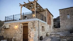 Ein Steinhaus mit einer Holztür, einem Balkon mit Metallgeländer und einer angrenzenden Steinmauer.