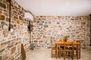 Um quarto com paredes de pedra, uma mesa de madeira e cadeiras, um aparelho de ar condicionado e um vaso com planta.