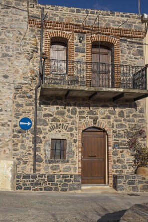 A stone building with a wooden door, a balcony with wrought iron railings, and a blue directional sign.