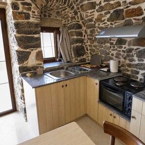 A kitchen with a stone wall, a window with curtains, a sink, a stove, and wooden cabinets.