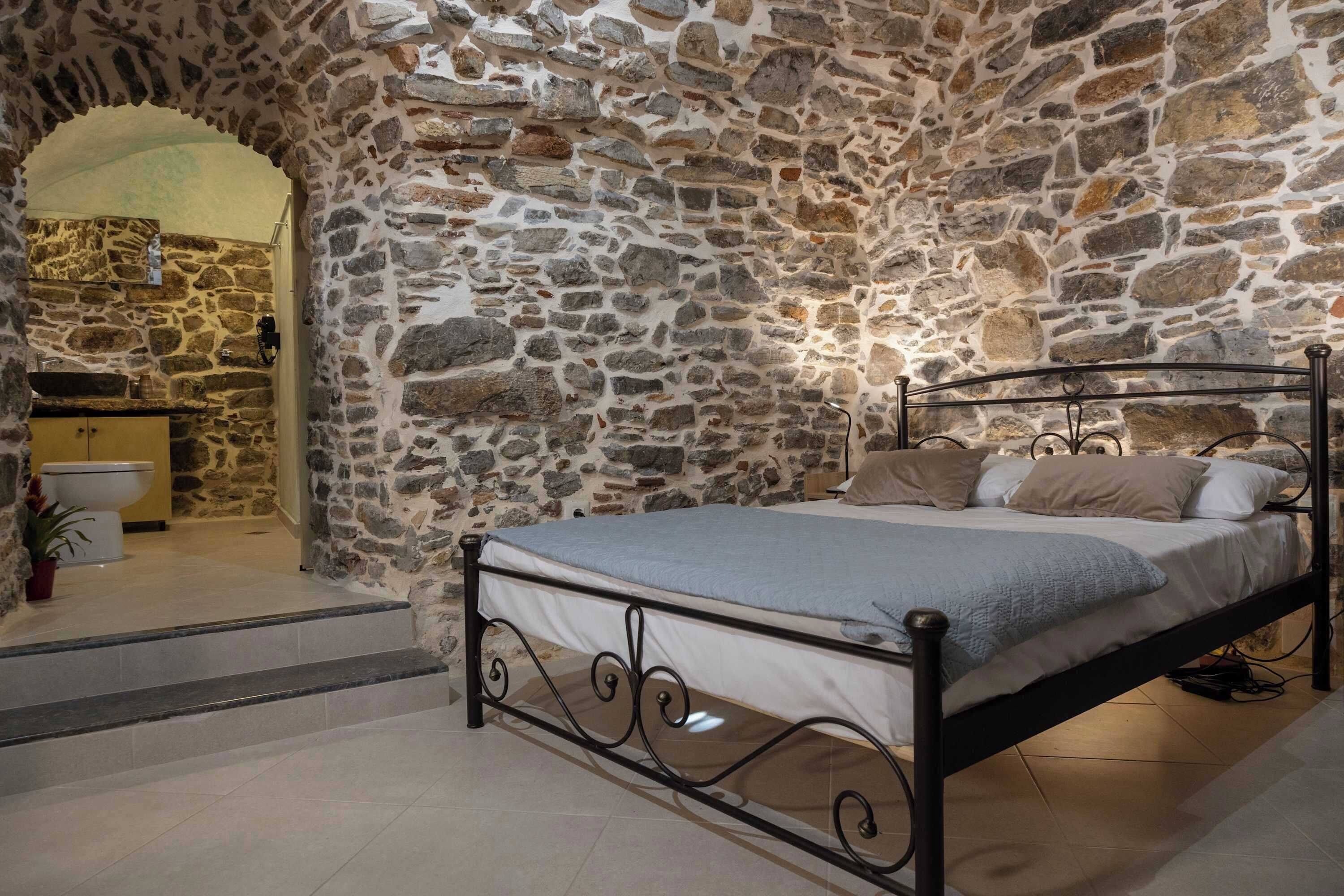 A bedroom with a stone wall, a bed with a metal frame, a small sink, and a potted plant.