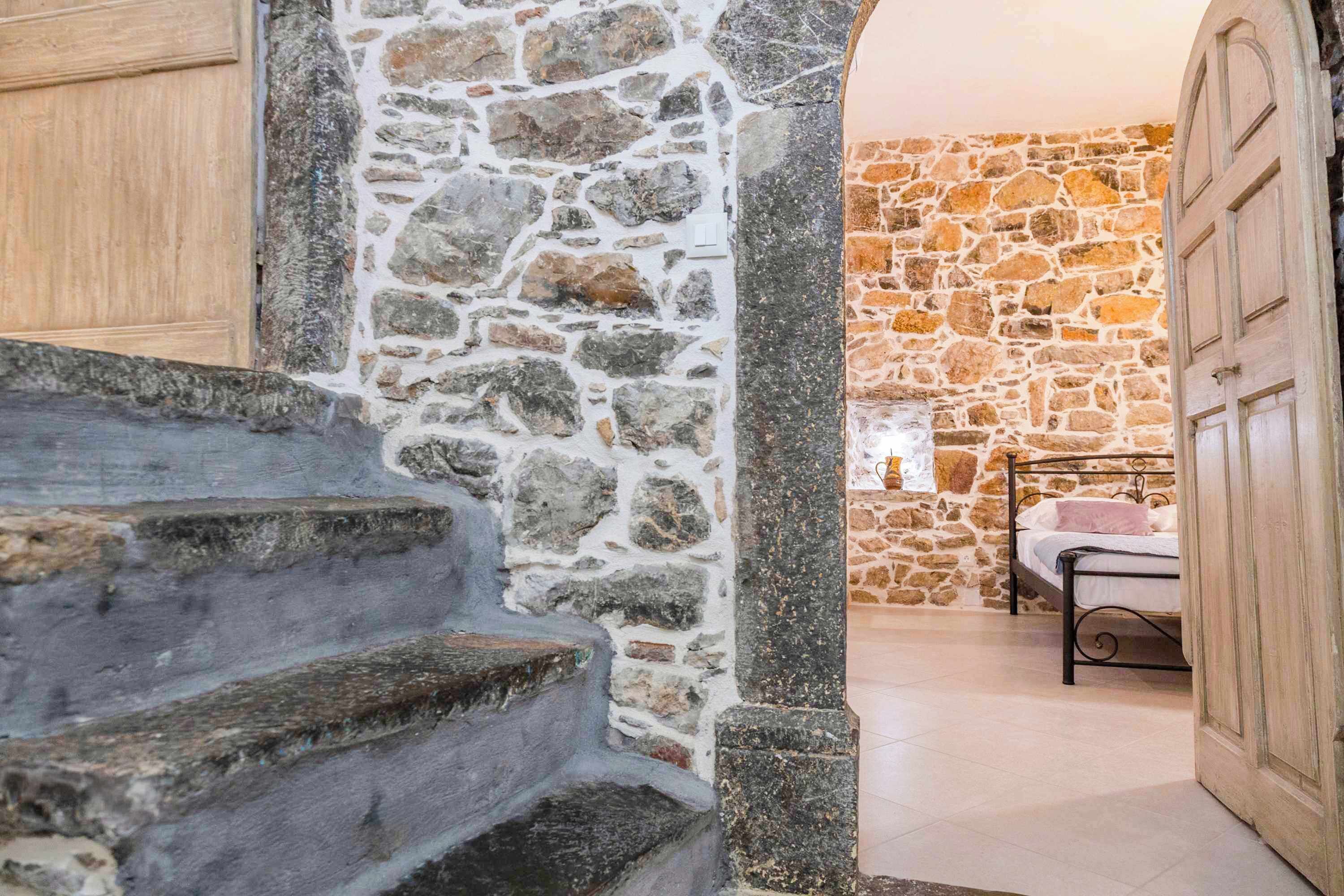 A stone staircase leading to a bedroom with a bed and a wooden door.