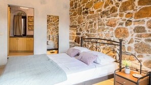 Een slaapkamer met een stenen muur, een bed met kussens, een nachtkastje met een lamp en een houten kast.