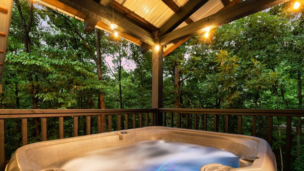 Un jacuzzi con terraza de madera y barandas, rodeado de árboles.