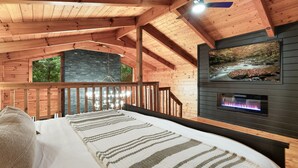Interior de una cabaña de madera con una cama, una chimenea de piedra y un mural paisajístico.