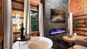 Una habitación acogedora con chimenea, televisor montado en la pared y una mesa redonda con una botella de vino.