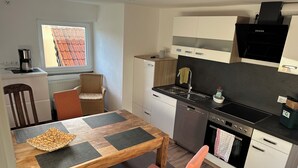 A compact kitchen with a dining area, including a table with placemats, chairs, a coffee maker, a dishwasher, and a stove.