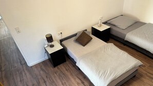 A bedroom with two beds, a nightstand with a lamp, and a power outlet on the wall.