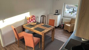 A compact living space with a dining table, two chairs, a coffee machine, a radiator, and a window with a view of buildings.