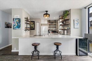 A modern kitchen with a central island, bar stools, and a built-in refrigerator.