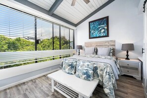 A bedroom with a bed, bench, bedside tables, and a window with blinds.