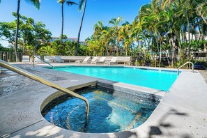 A swimming pool with a hot tub, surrounded by lounge chairs and palm trees.