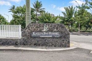 A sign for Kailua Bay Resort Condominiums with a stone wall background and palm trees.