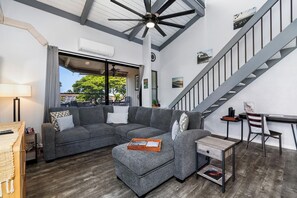 A modern living room with a sectional sofa, a small table, a desk, and a staircase.