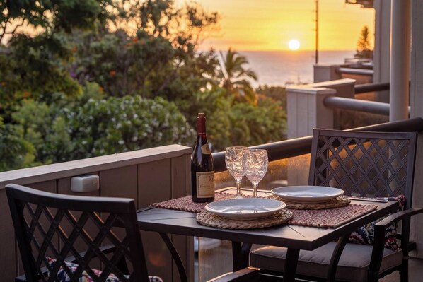 A table set for two with a bottle of wine and two glasses, overlooking a sunset over the ocean.