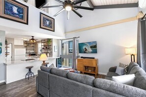 Ein modernes Wohnzimmer mit einem grauen Sofa, einem Fernseher und einem Deckenventilator.