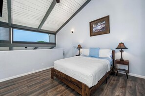 Ein Schlafzimmer mit einem großen Bett, zwei Nachttischen, einem Fenster und einer Decke mit Holzbalken.