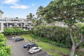 A parking lot with several cars, a building with a modern design, and lush greenery including palm trees.