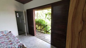 A bedroom with a bed, a door leading to a balcony, and a view of greenery outside.