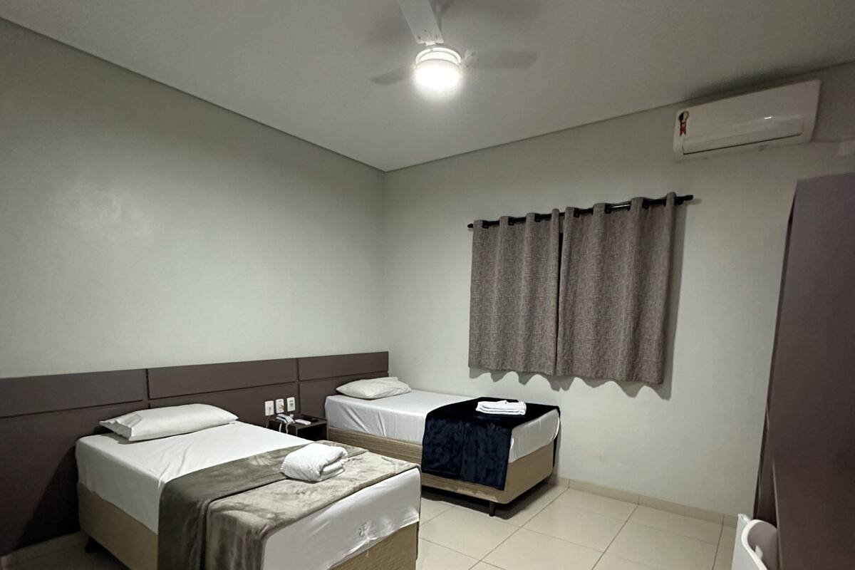 Ein Hotelzimmer mit zwei Betten, einem Deckenventilator, einer Klimaanlage und einem Vorhang.