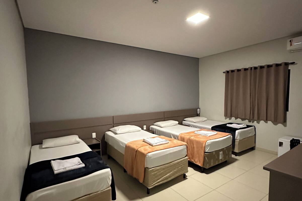 Ein Hotelzimmer mit vier Einzelbetten, einem Schreibtisch und einem Stuhl.