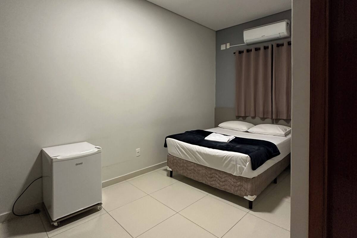 Ein kleiner, sauberer Raum mit einem Bett, einem Heizkörper und einem Fenster mit Vorhängen.