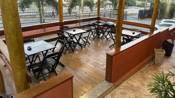 Een openluchtrestaurant met houten tafels en stoelen, een 'Welcome'-bord en uitzicht op de straat en palmbomen.