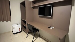 Een compacte kamer met een ingebouwd bureau, een aan de muur bevestigde televisie en een kleine koelkast.