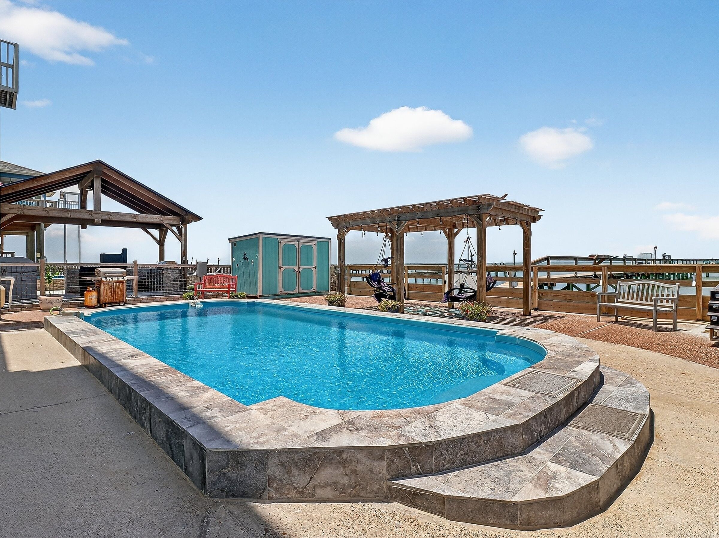 A swimming pool with a wooden deck, a gazebo, and a small building.