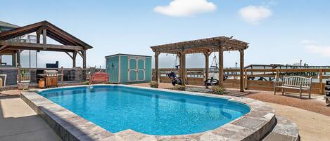 A swimming pool with a wooden deck, a gazebo, and a small building.