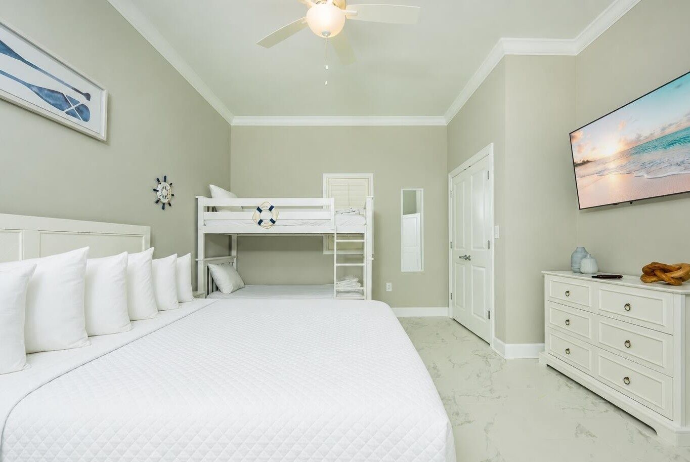 A bedroom with a bunk bed, a ceiling fan, a dresser, and a painting on the wall.