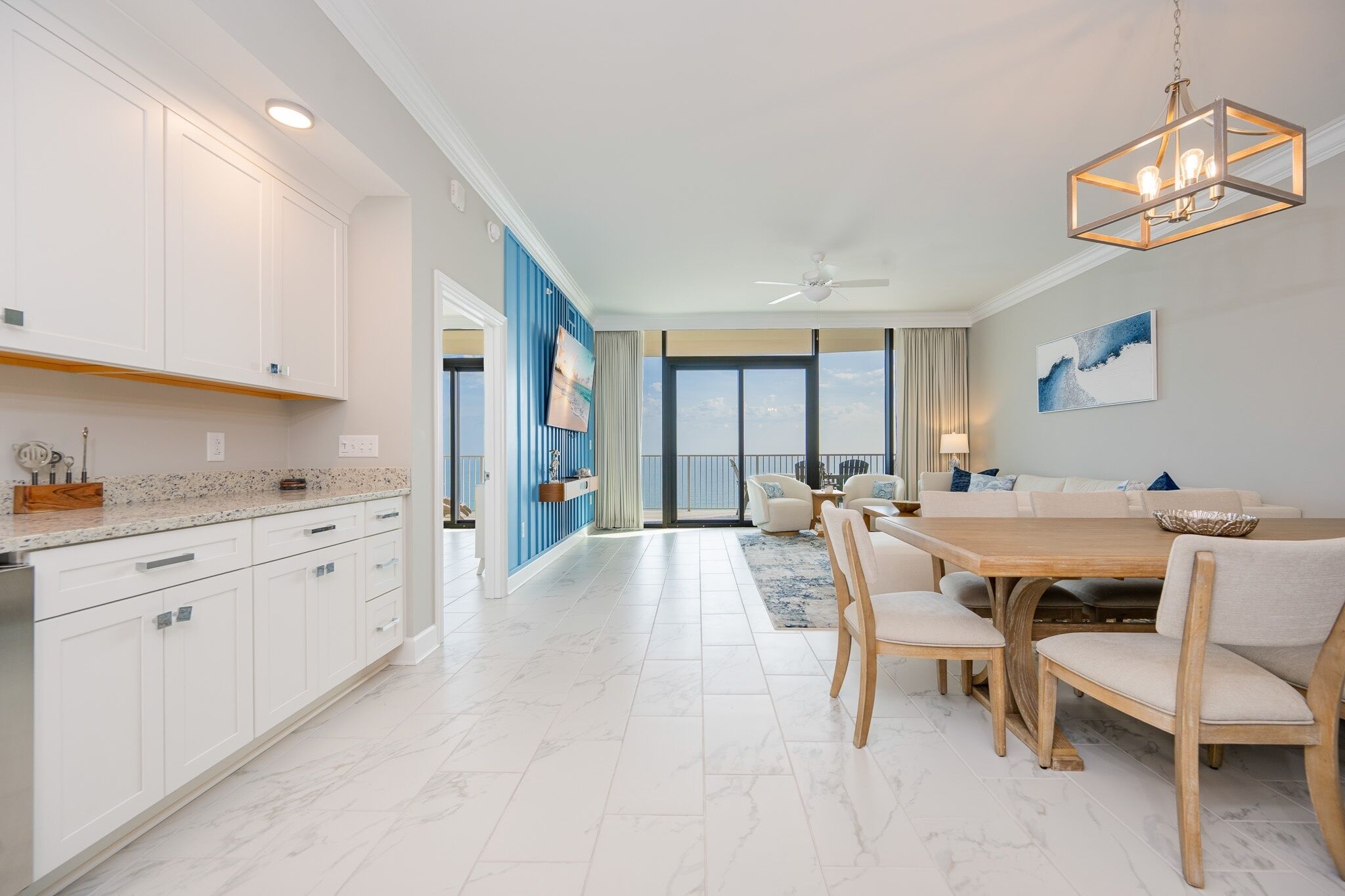 A modern kitchen with white cabinets, a marble countertop, and a dining area with a wooden table and chairs.
