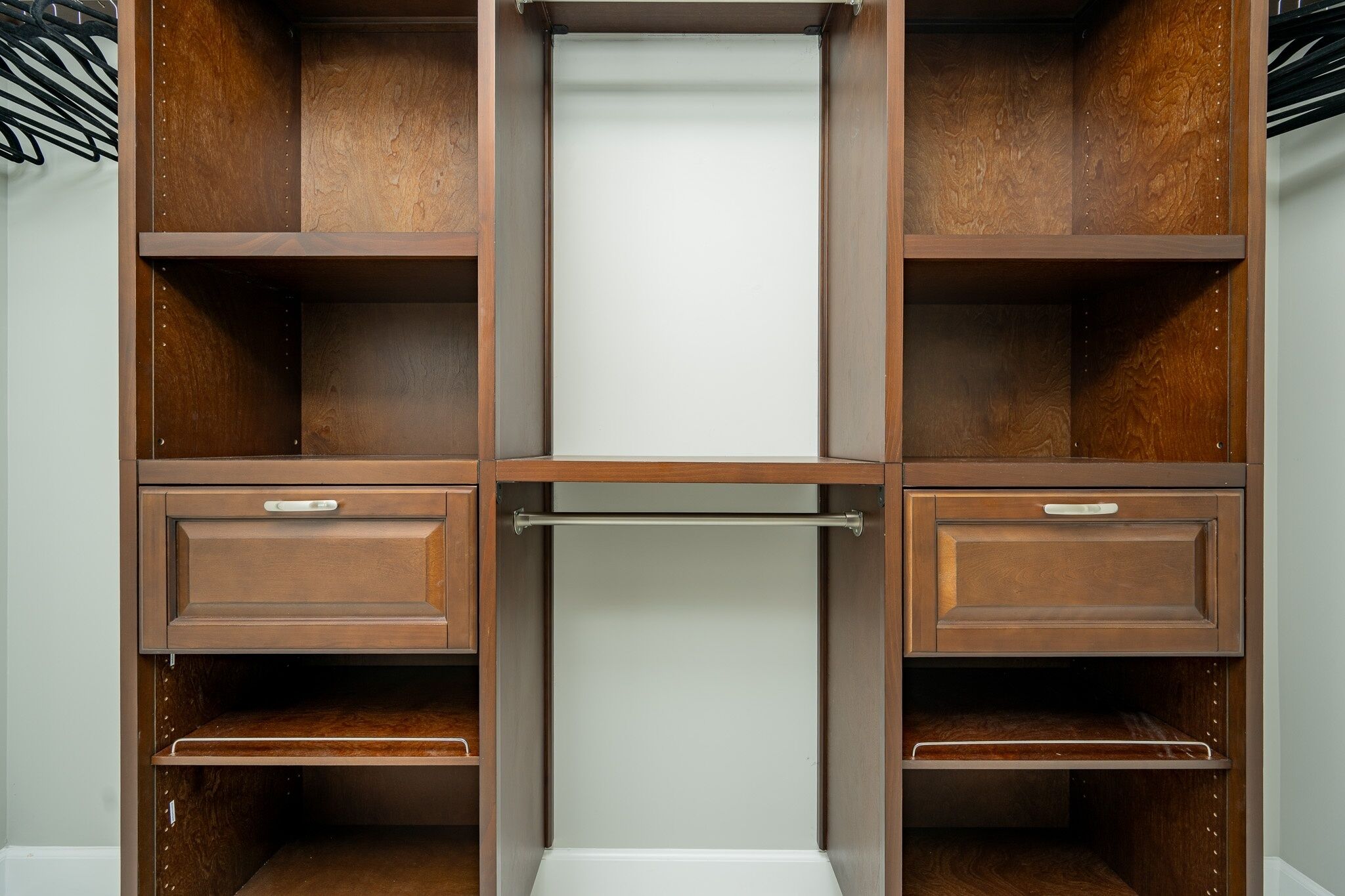 A wooden wardrobe with multiple shelves and drawers, featuring a central hanging rod.