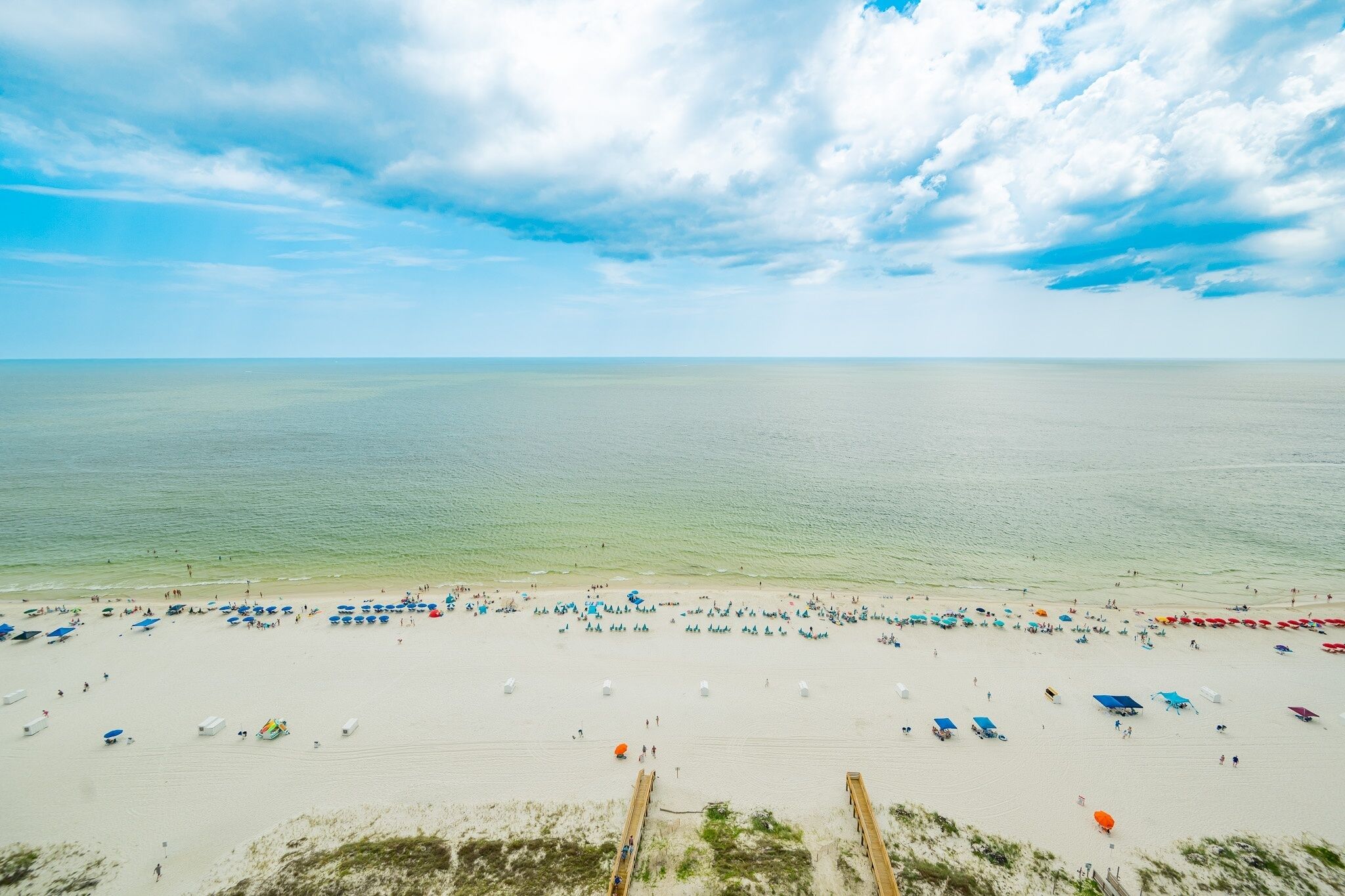 A beach with rows of umbrellas and beach chairs, a wooden walkway, and the ocean in the background.