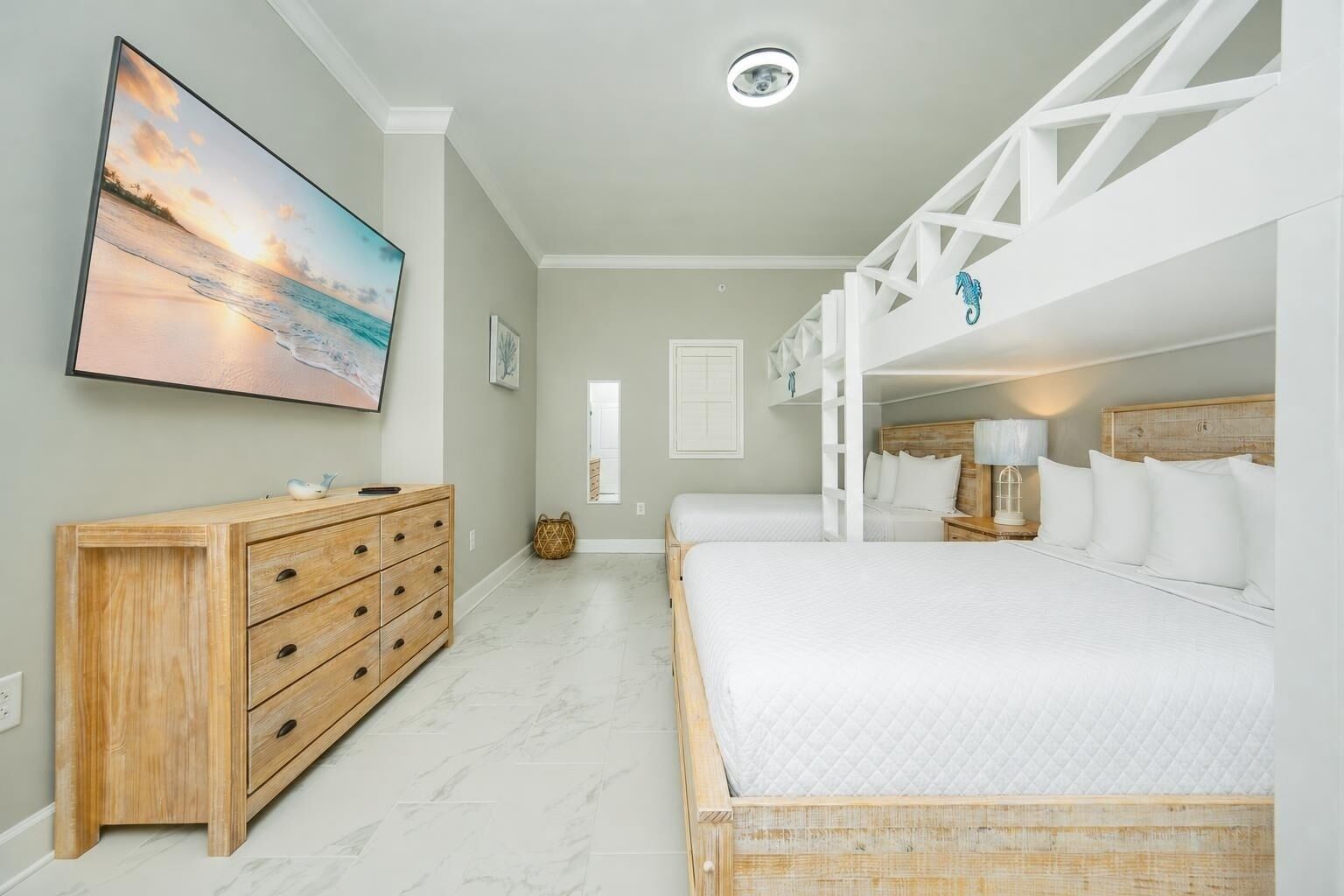 Un dormitorio con una cama, un aparador de madera, un televisor montado en la pared y una cama litera.