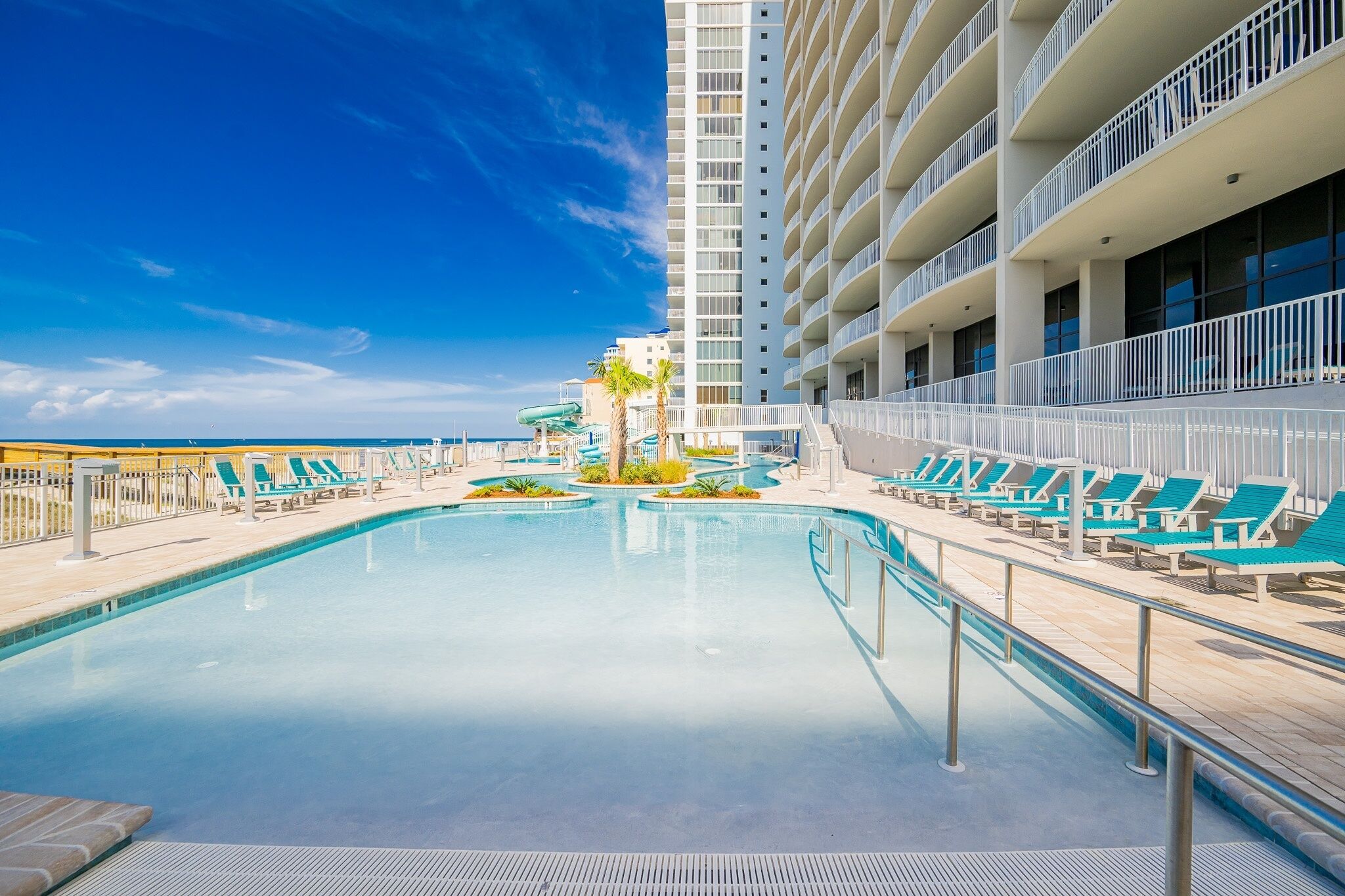 A pool area with lounge chairs, a water slide, and a tall building with balconies.
