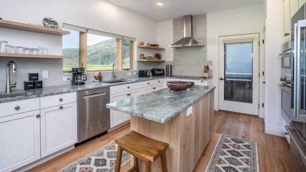 A modern kitchen with white cabinets, a granite countertop, a stainless steel dishwasher, and a large island with a bowl.